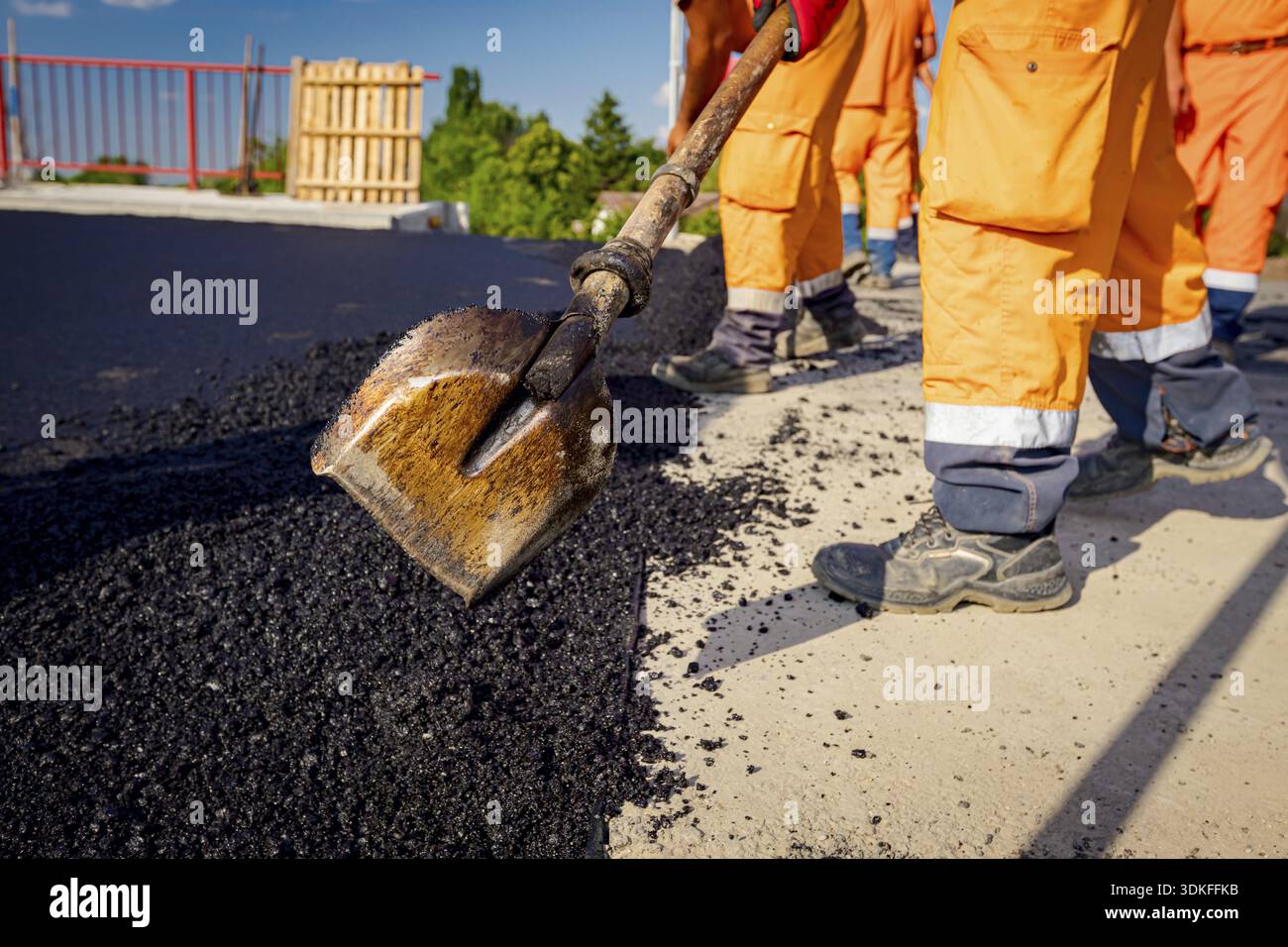 Peu de travailleurs utilisent des pelles pour niveler, mettent en place une couche de tarmac frais aux bonnes mesures, versent de l'asphalte chaud Banque D'Images