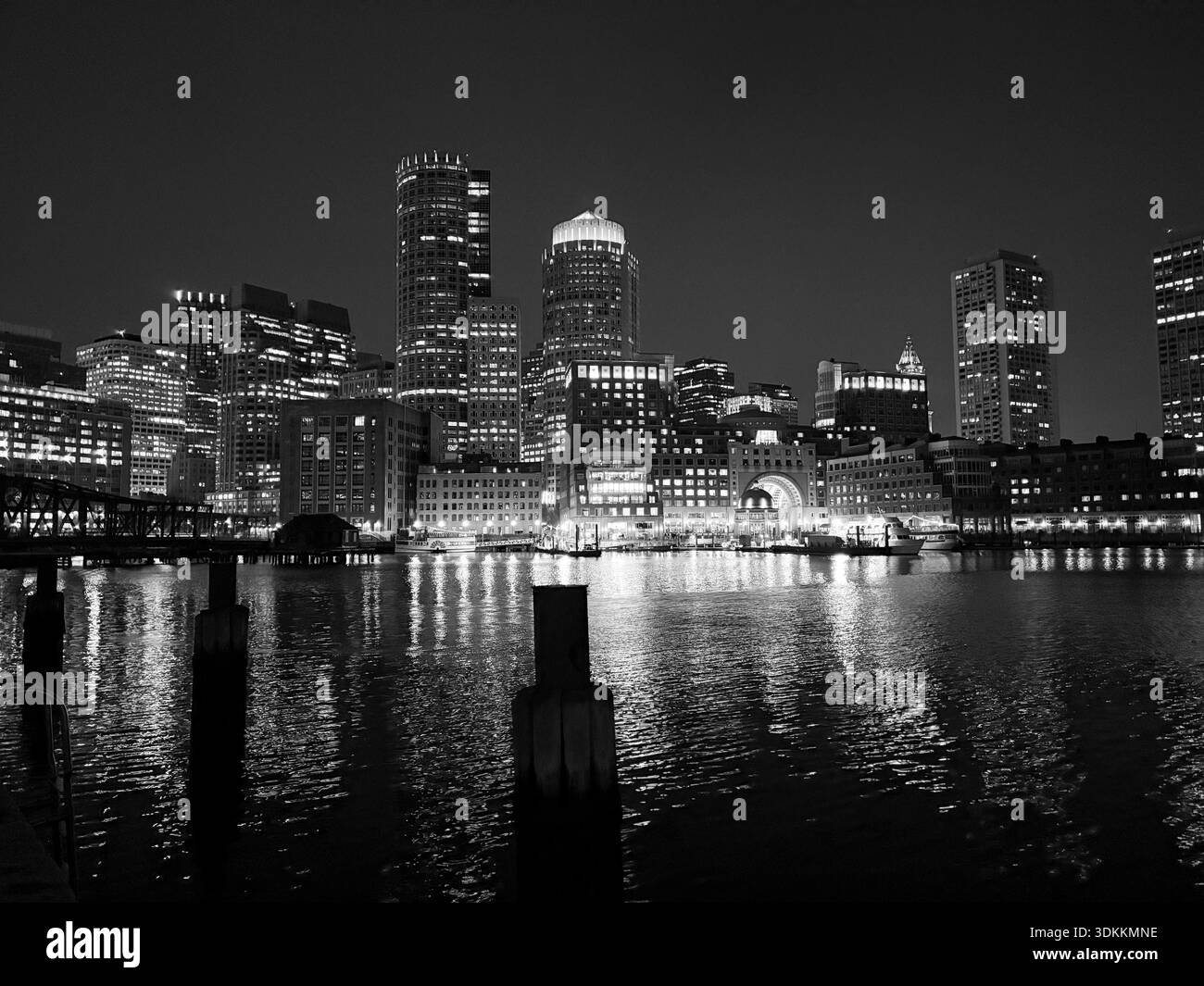 Boston Harbor montre les bâtiments de la ville éclairés la nuit avec des reflets dans l'eau. Banque D'Images