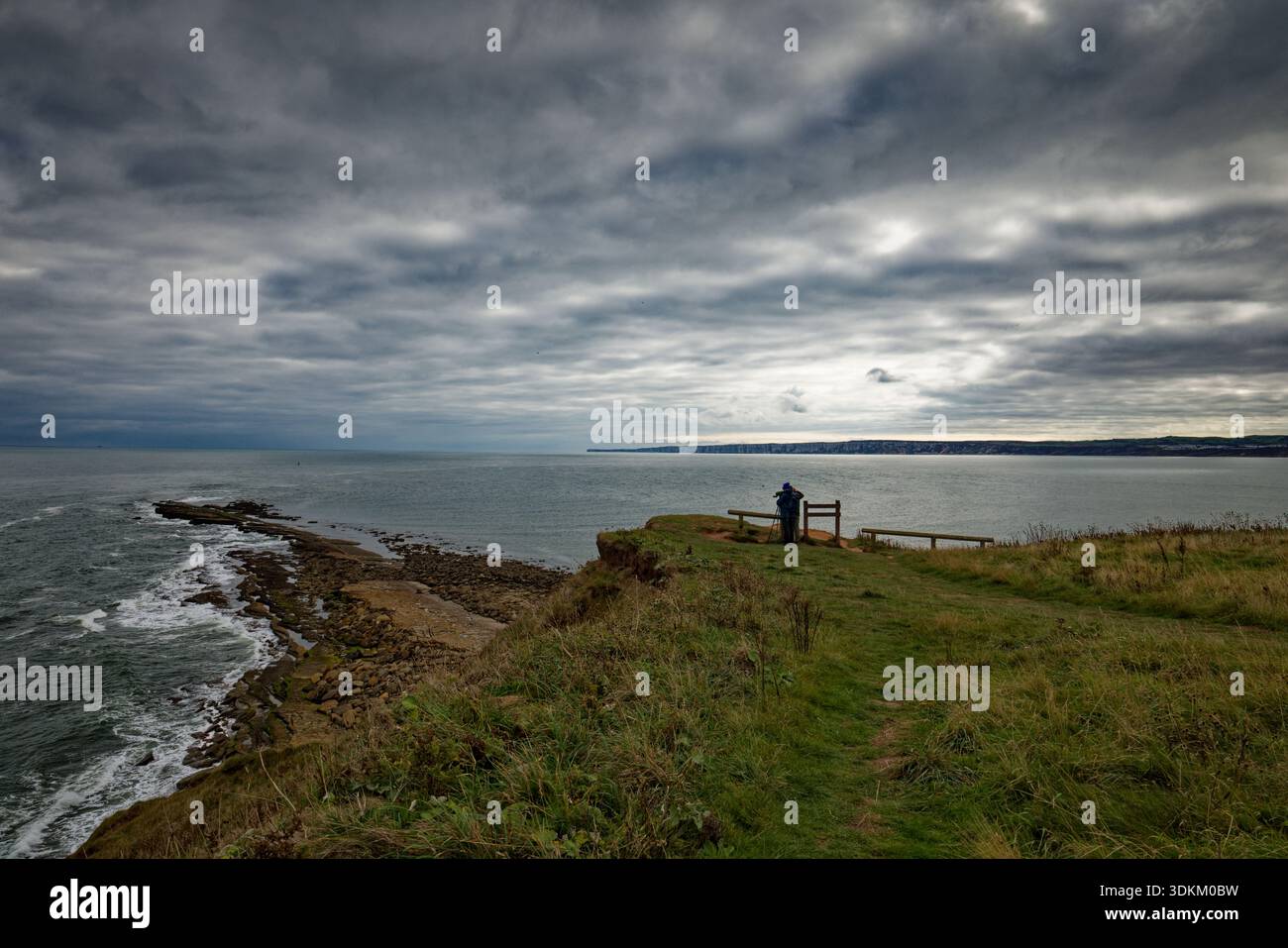 Une paire d'observateurs d'oiseaux regardent à travers un télescope dans la mer du Nord par une journée sombre depuis la falaise de Filey Brigg, dans le Yorkshire du Nord. Banque D'Images