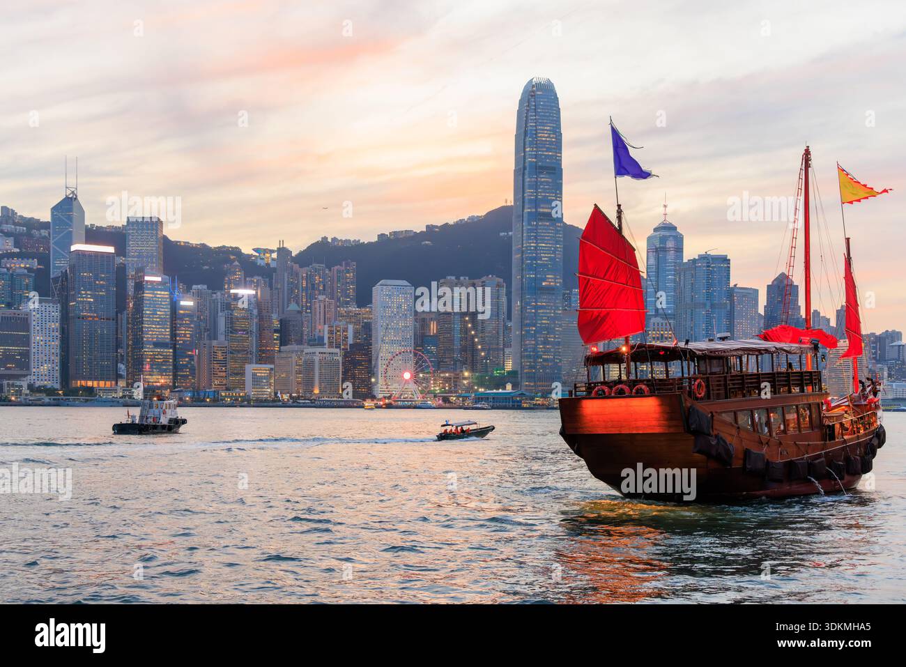 Jonque traditionnelle en bois avec des voiles rouges contre Hong Kong skyline pendant le coucher du soleil, scène urbaine emblématique Banque D'Images
