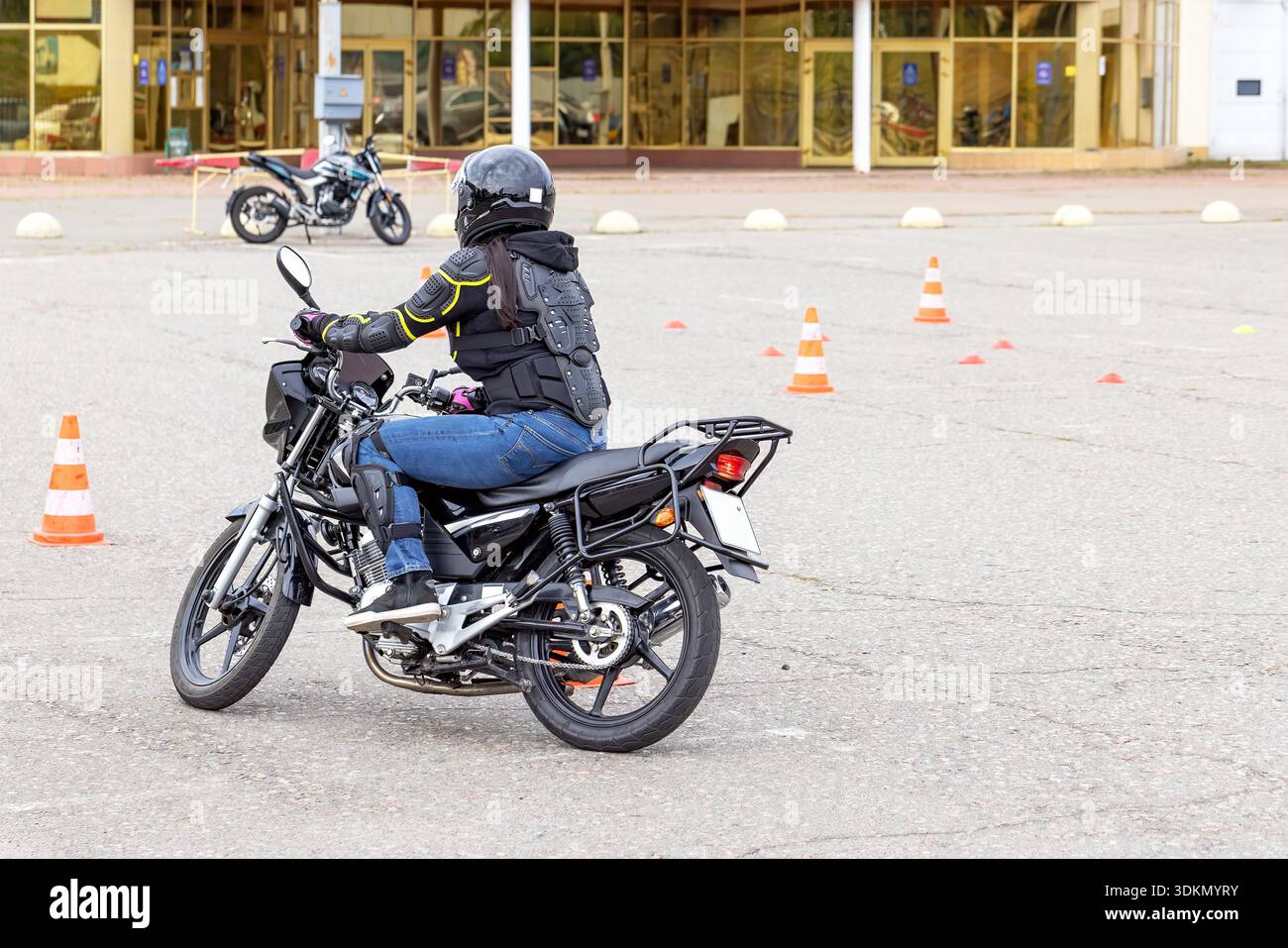 Motard manœuvre à travers un parcours rempli de cônes de circulation, en se concentrant sur l'équilibre et le contrôle. La journée ensoleillée améliore l'atmosphère d'apprentissage, créant Banque D'Images