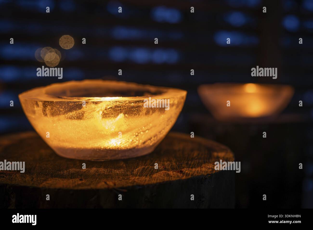 Bols de glace éclairés par des bougies de thé allumées se tiennent sur les troncs d'arbre, hiver, Finlande Banque D'Images
