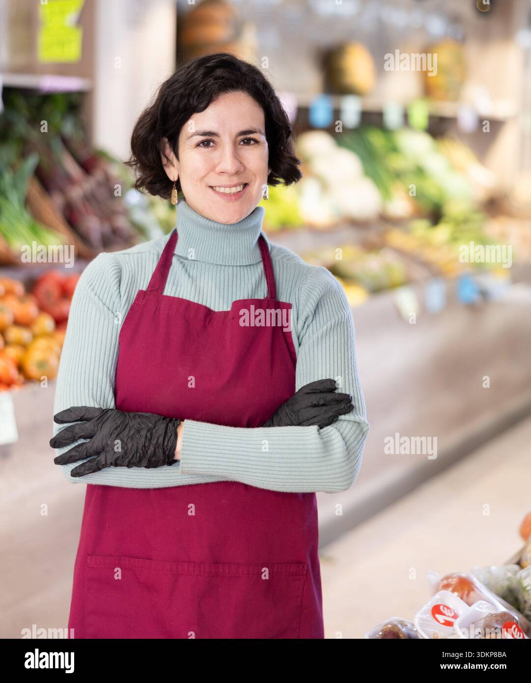 Employé de magasin de femme dans le tablier et les stands de gants dans la zone de vente de légumes Banque D'Images