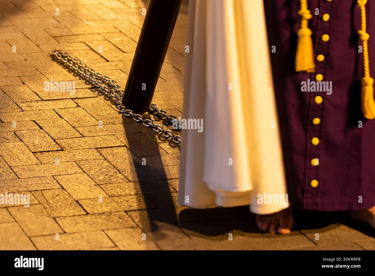 La personne se tient debout en tenue traditionnelle lors d'un événement en soirée, avec une chaîne visible couchée sur le sol à proximité. Banque D'Images