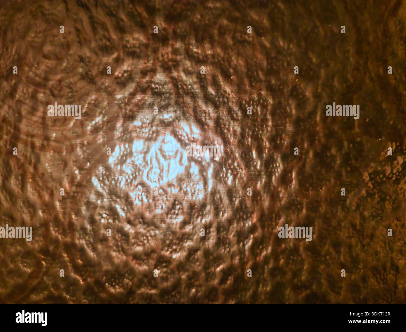 Vue macro de verre ambré texturé à Budapest avec ondulations circulaires concentriques. Il est doté d'une lumière chaude et dorée provenant d'une source lumineuse centrale. Idéal pour retr Banque D'Images