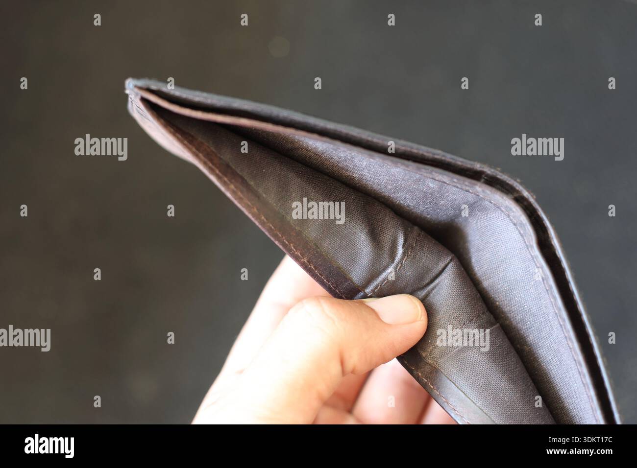 Gros plan de la main tenant un portefeuille en cuir noir vide : concept de crise financière, de pauvreté et de manque d'argent sur un fond sombre Banque D'Images