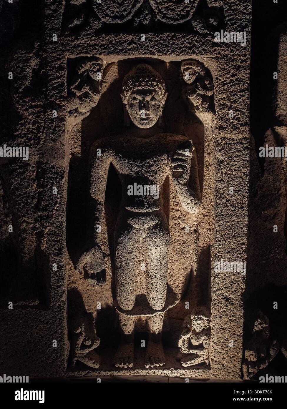 Ajanta, Inde - 26 décembre 2025 : vue d'une ancienne figure sculptée debout résolument dans une alcôve de pierre, des ombres dansant sur sa surface texturée Banque D'Images