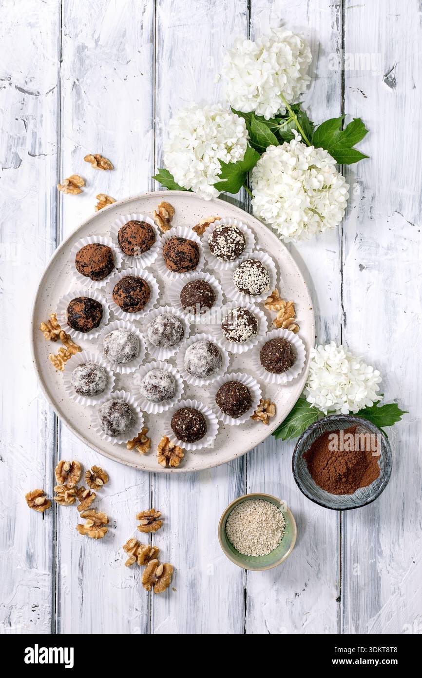 Vue de dessus boules énergétiques végétaliennes crues au chocolat maison ou truffes avec des graines de sésame en poudre de cacao et des noix sur fond de bois blanc avec hydrangea fl Banque D'Images