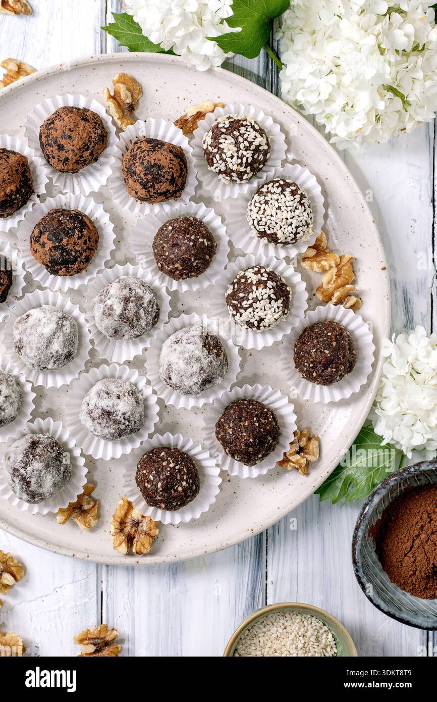 Assortiment de boules végétaliennes crues au chocolat maison truffes dans des gobelets en papier sur une assiette en céramique. Différents enrobages : poudre de cacao sucre en poudre graines de sésame. Déc Banque D'Images