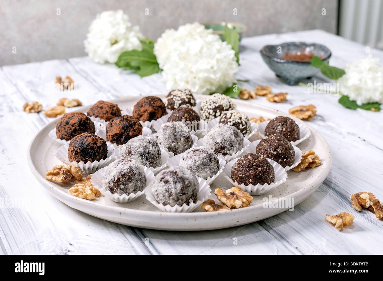 Boules végétaliennes crues au chocolat maison variété de truffes avec différentes garnitures sur plaque en céramique blanche. Saupoudré de graines de sésame en poudre de cacao. Décoré w Banque D'Images