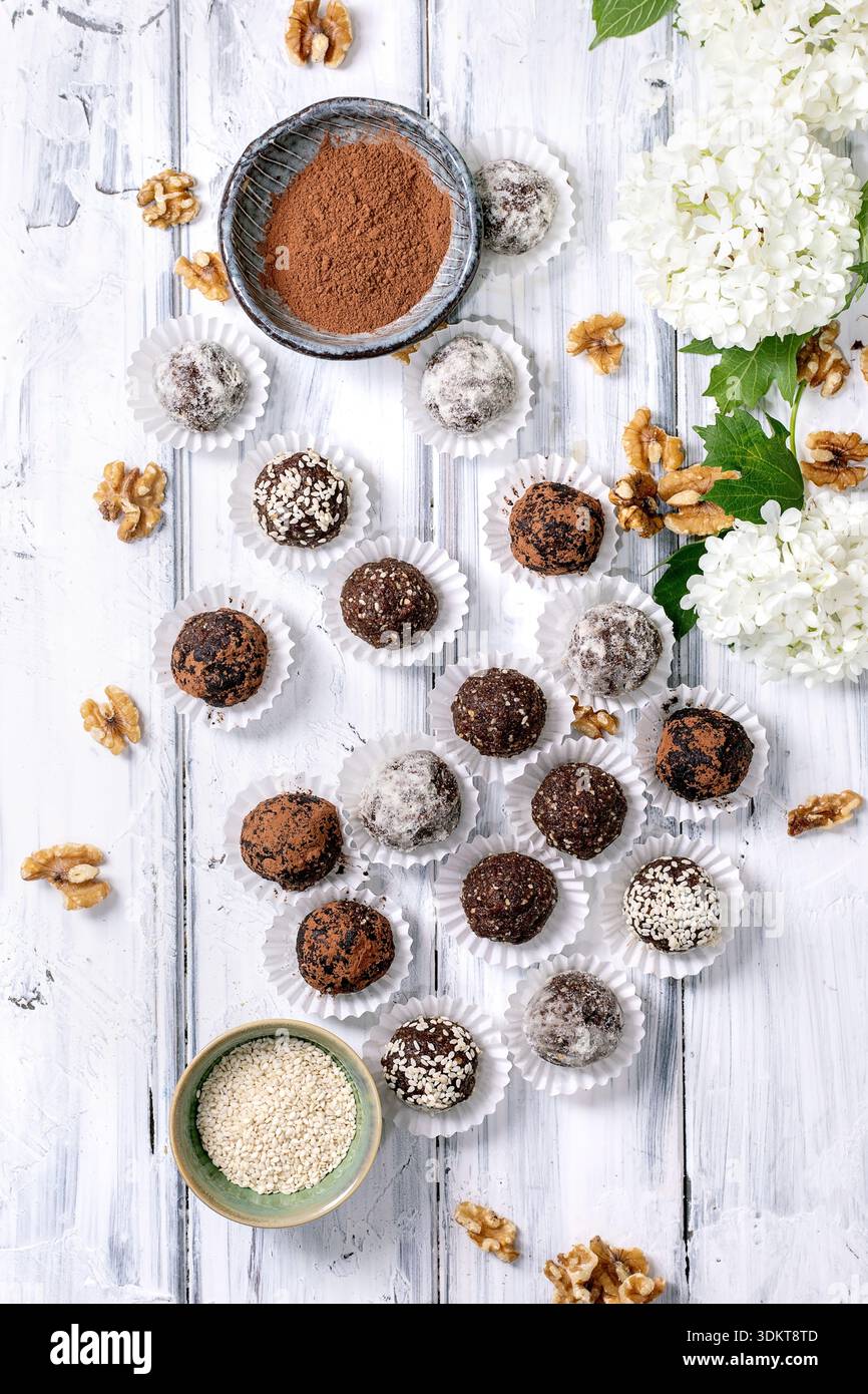 Boules végétaliennes crues au chocolat maison truffes dans des gobelets en papier cacao en poudre graines de sésame noix et fleurs d'hortensia blanches sur backgro en bois blanc rustique Banque D'Images