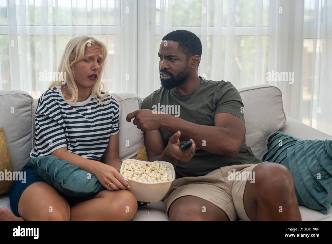 Jeune couple regardant la télévision ensemble, partageant du pop-corn et réagissant à un film ou à une émission sportive, divertissement occasionnel à la maison et relation Banque D'Images