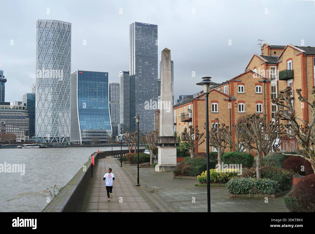 Un coureur solitaire sur le chemin Riverside à Rotherhithe, Londres, Royaume-Uni montrant Canary Wharf au-delà de l'obélisque érigé dans le cadre du développement. Banque D'Images