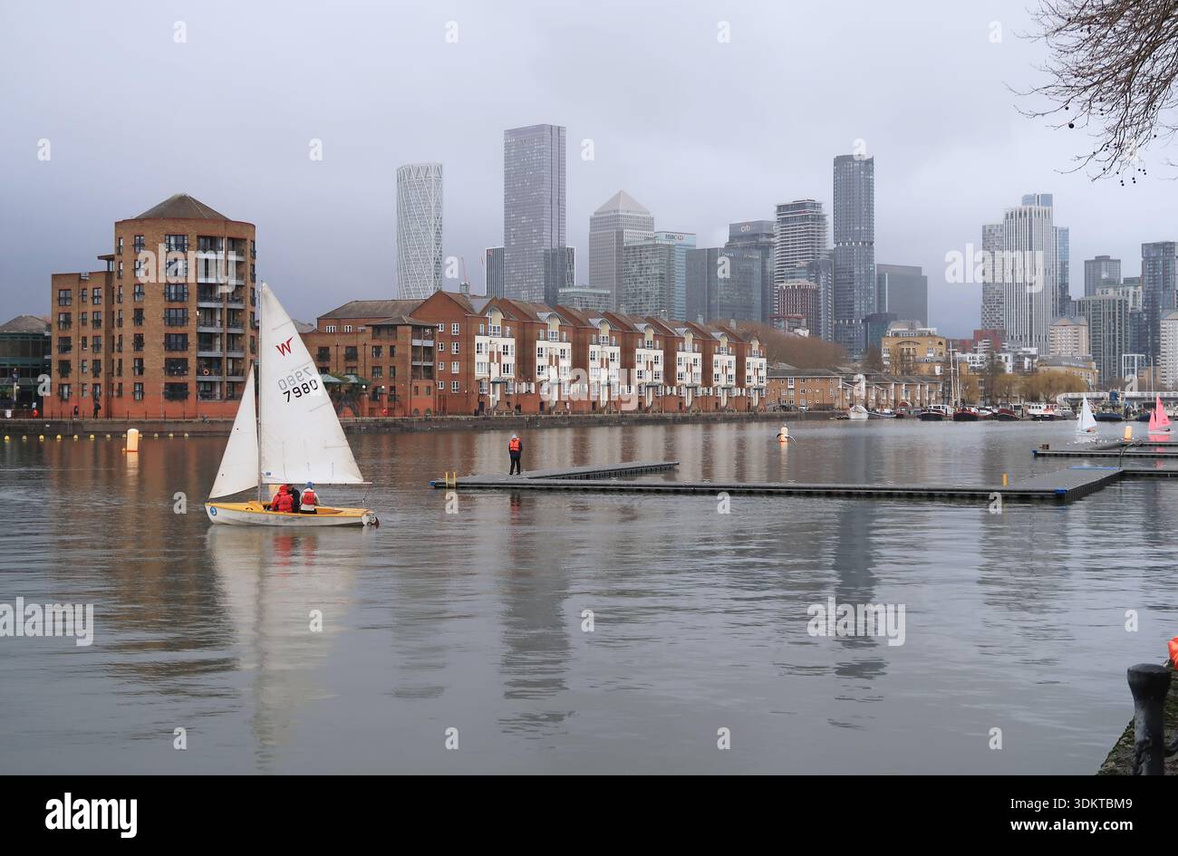 Une voile dingy sur Greenland Dock, qui fait partie des anciens Surrey Docks dans le sud-est de Londres, au Royaume-Uni. Tours de Canary Wharf en arrière-plan. Banque D'Images