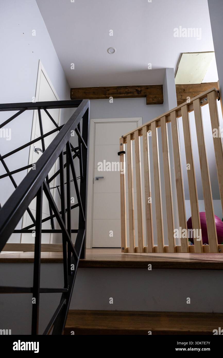 Escalier intérieur avec une balustrade en métal noir aux motifs géométriques, une balustrade en bois à lattes verticales et une porte blanche encadrée par du bois. Banque D'Images