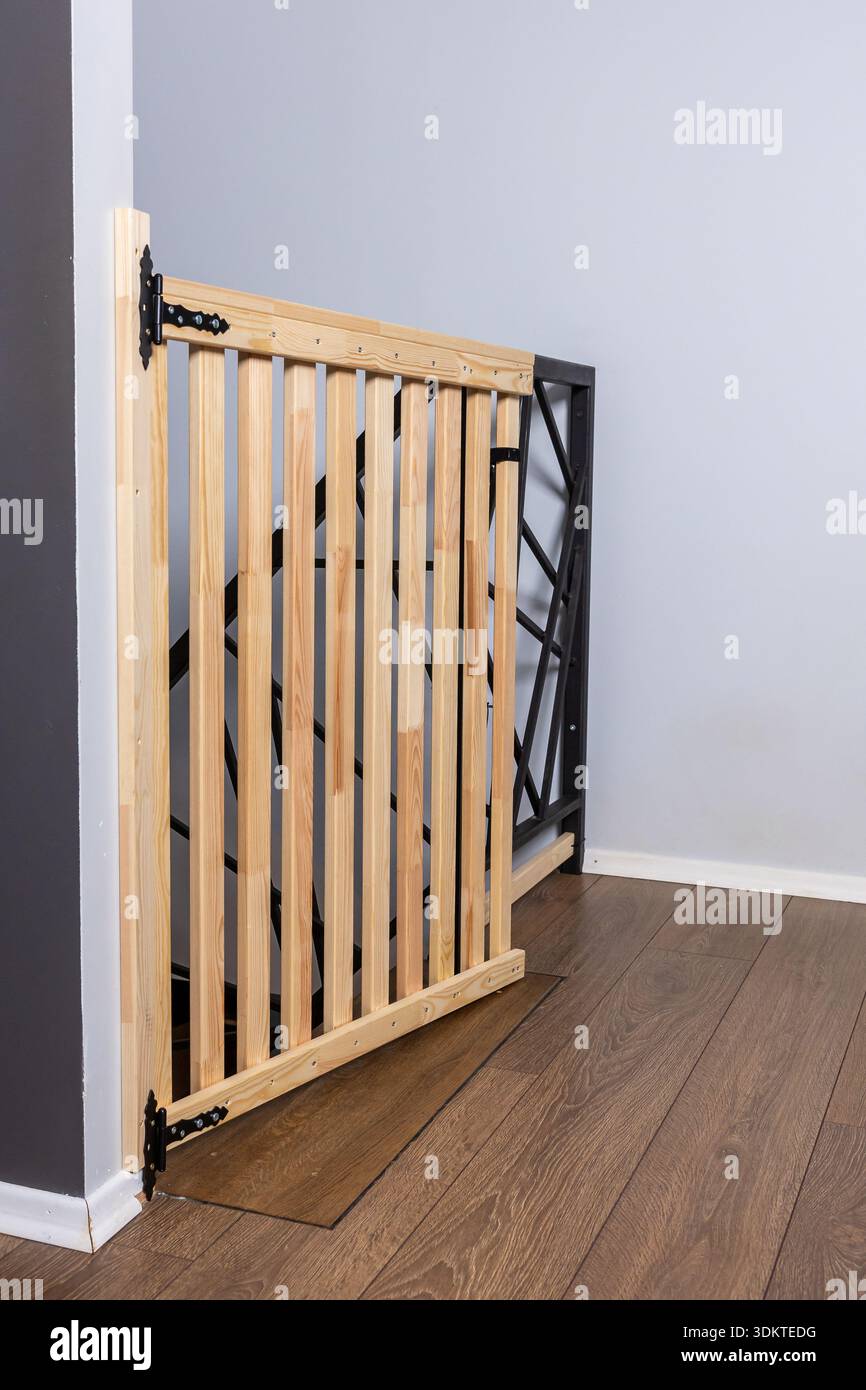 Barrière de sécurité en bois avec lattes verticales et charnières en métal noir en haut d'un escalier. Comprend des balustrades géométriques, des planchers de bois et des murs gris. Banque D'Images