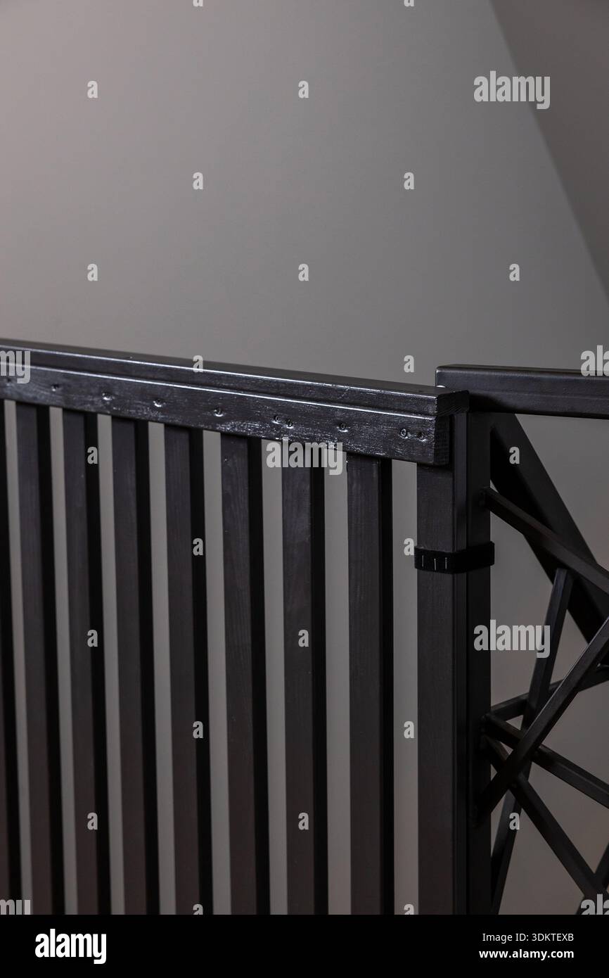 Garde-corps en métal noir avec des lattes verticales et un design géométrique sur la droite, fixé avec des vis, sur un fond de mur gris Uni. Banque D'Images