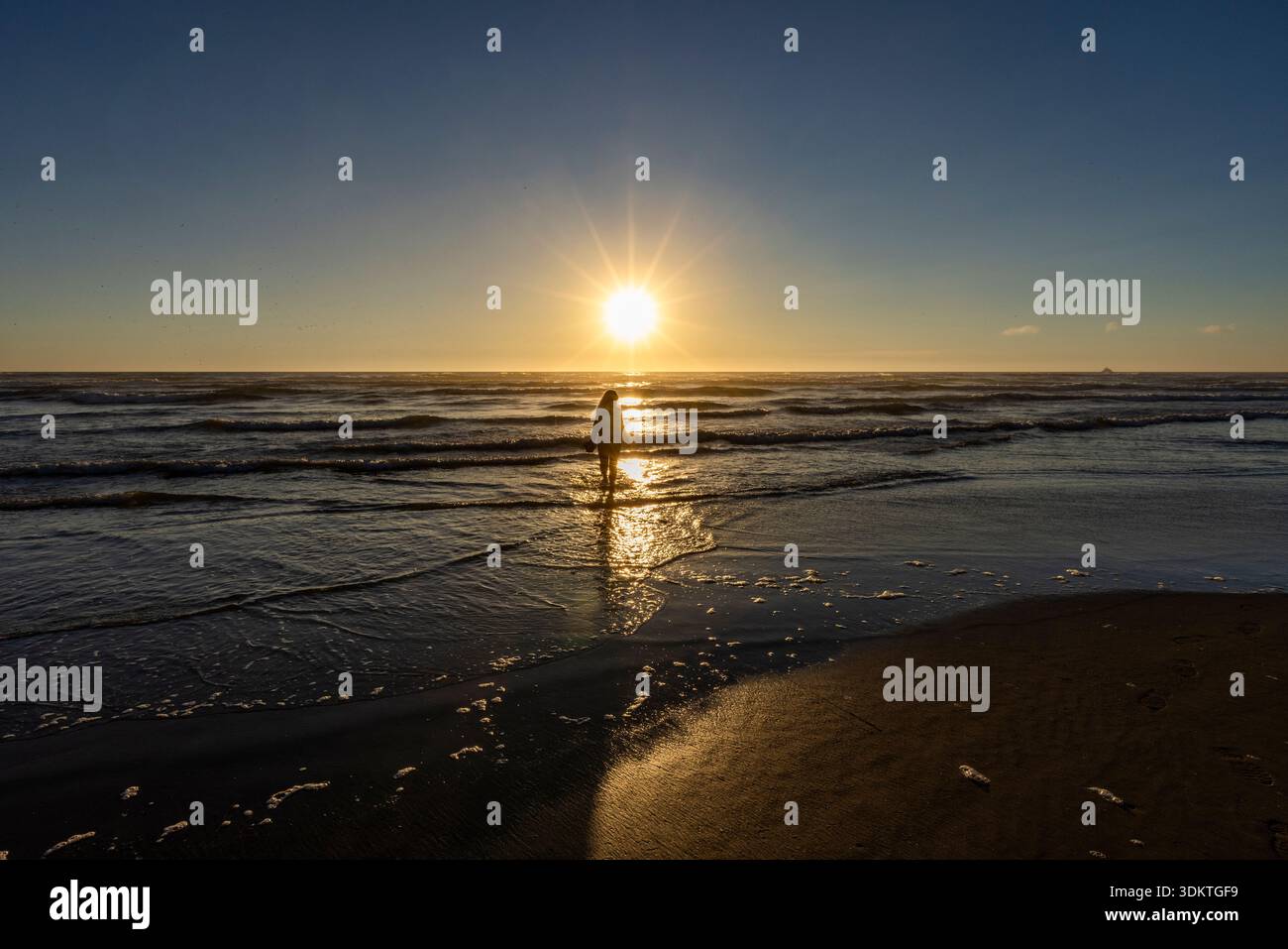 USA, Oregon, Cannon Beach, femme pataugant dans le surf au coucher du soleil Banque D'Images