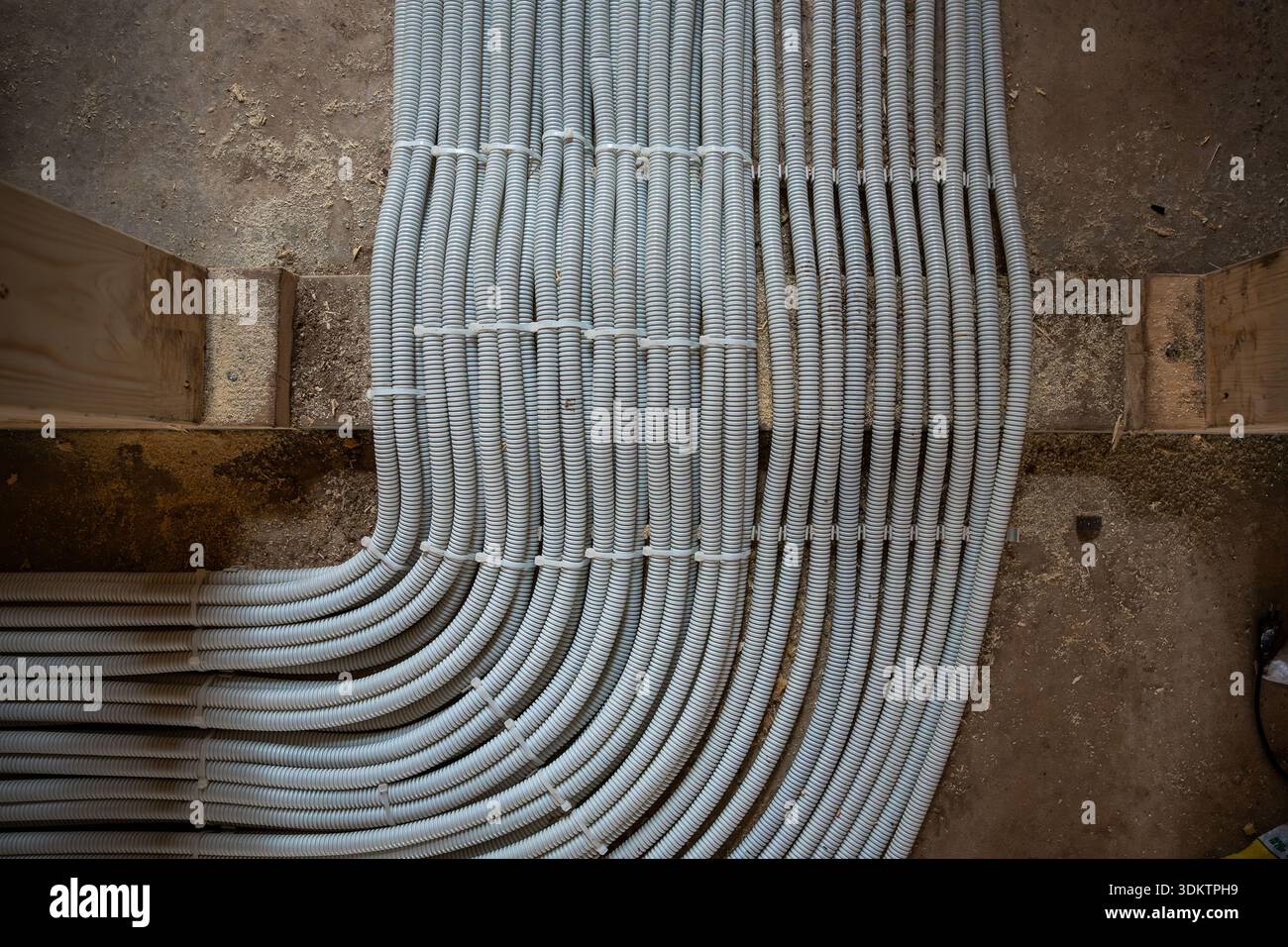 Vue détaillée des conduits de ventilation annelés blancs sur sol en béton avec ossature en bois, montrant les premières étapes de construction et la planification technique. Banque D'Images