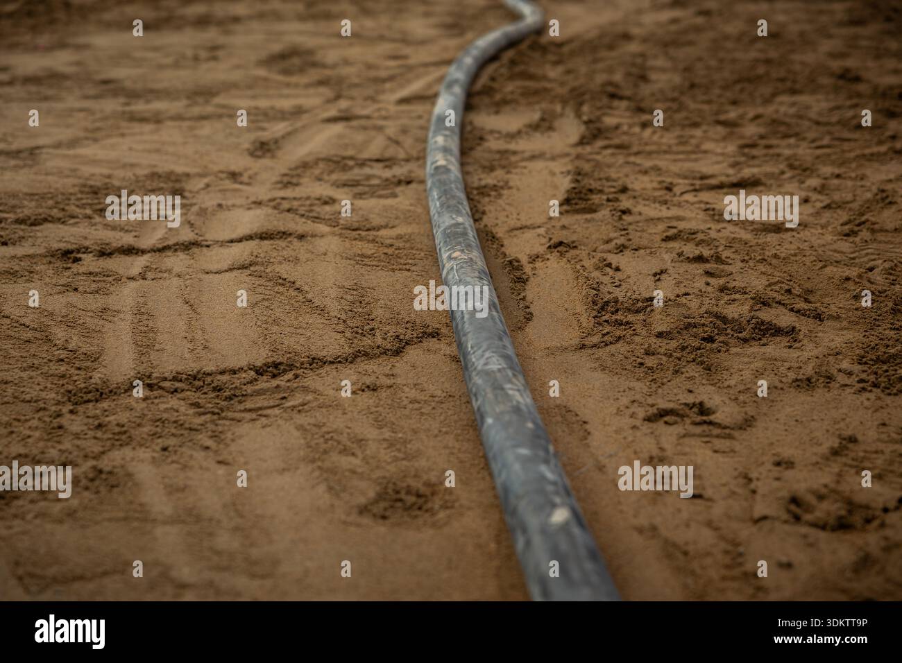 Un seul tuyau de chauffage par le sol se courbe sur du sable ou du sol compacté, avec des textures et des marques de sol visibles, soulignant les premières étapes de construction. Banque D'Images