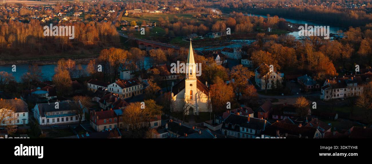 Vue aérienne en fin d'après-midi de Kuldiga, Lettonie, flèche de l'église au-dessus des toits rouges, rues pavées, arbres d'automne, rivière Venta et Ventas Rumba, longues ombres Banque D'Images