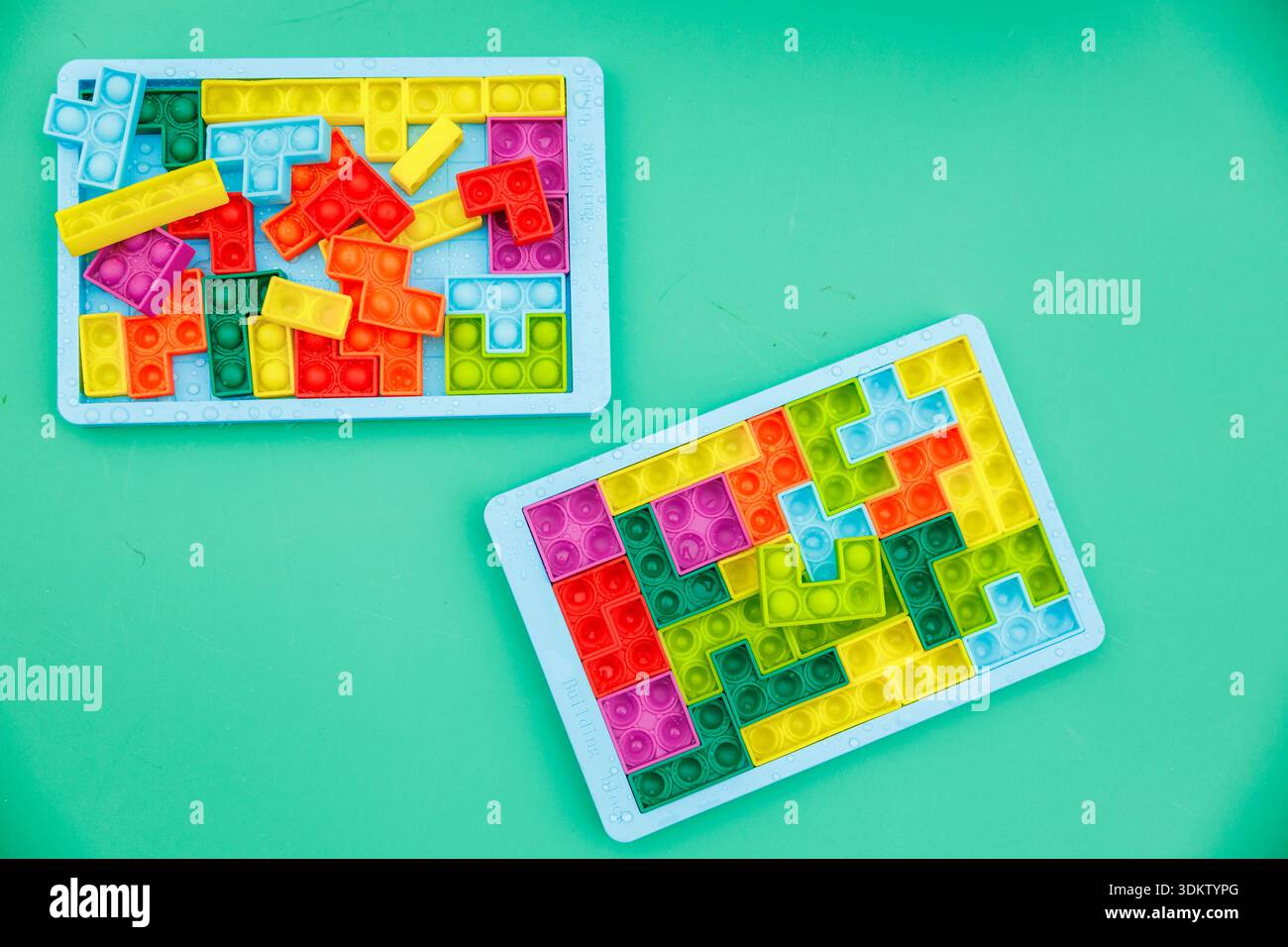 Plateaux bleu pastel avec blocs de puzzle pop it en silicone multicolore. Deux plateaux sont assis sur sarcelle, un éparpillé et un presque résolu avec le jaune entrelacé Banque D'Images
