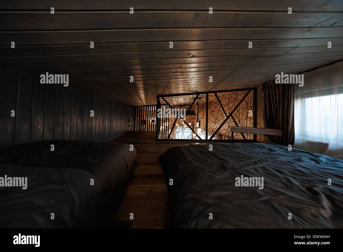 Loft à plafond bas avec deux matelas doubles en couette foncée dans une allée étroite. Barrière de fil et de bois et cadre de balustrade à lattes une ouverture comme luge pendante Banque D'Images