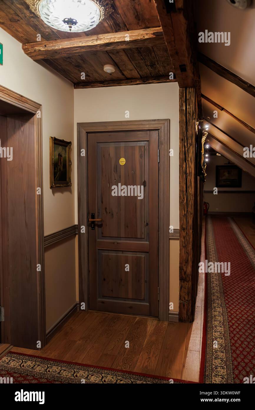 Confortable couloir d'hôtel rustique avec une perspective de point à la porte en bois. Lampes chaudes lumière poutres en bois, moulure sculptée, coureur, peinture et panneau de sortie i. Banque D'Images