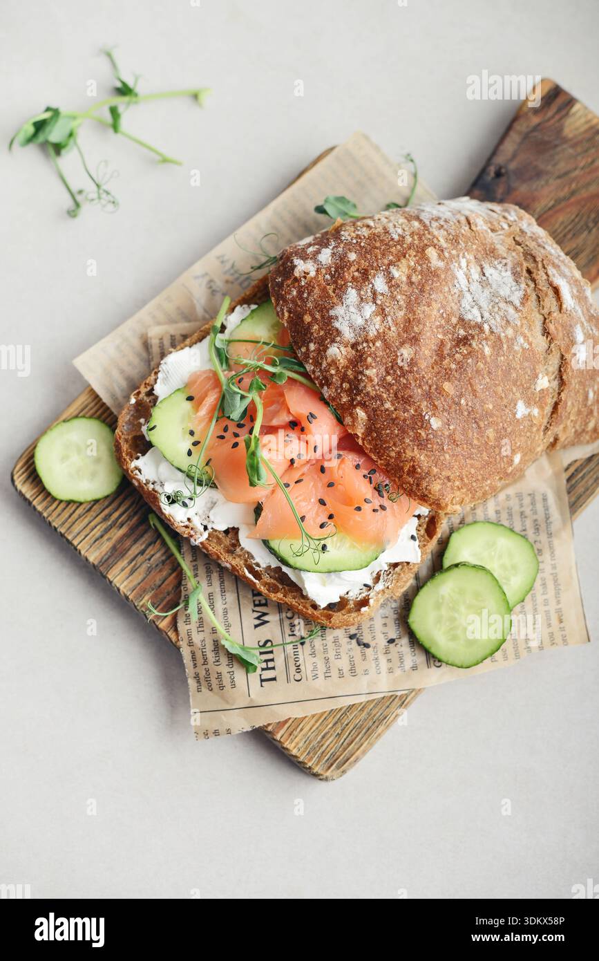 Sandwich au pain de seigle avec saumon salé, concombre, légumes verts et fromage à la crème sur planche à découper en bois gros plan Banque D'Images