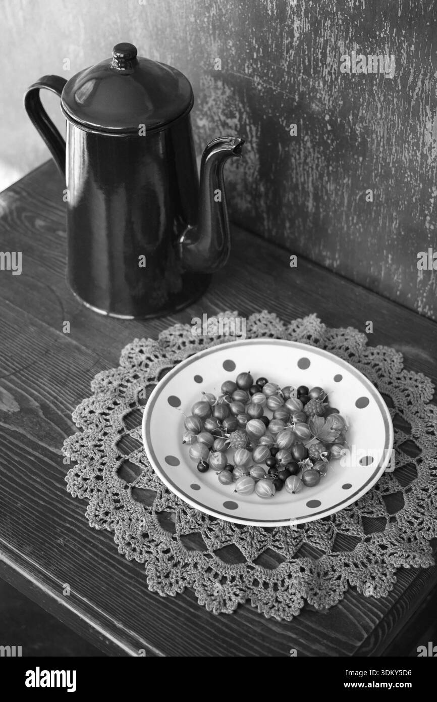 Vintage coffee pot émaillé et l'assiette de fruits de jardin sur la serviette décorative en bonneterie. Nature morte noir et blanc Banque D'Images