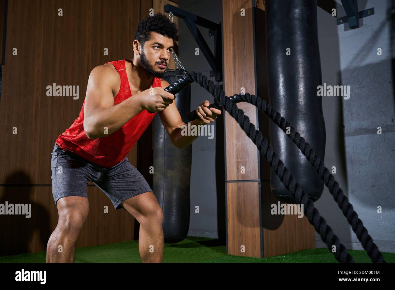 Un jeune sportif afro-américain dévoué se concentre sur son entraînement en utilisant des cordes de combat à l'intérieur. Banque D'Images