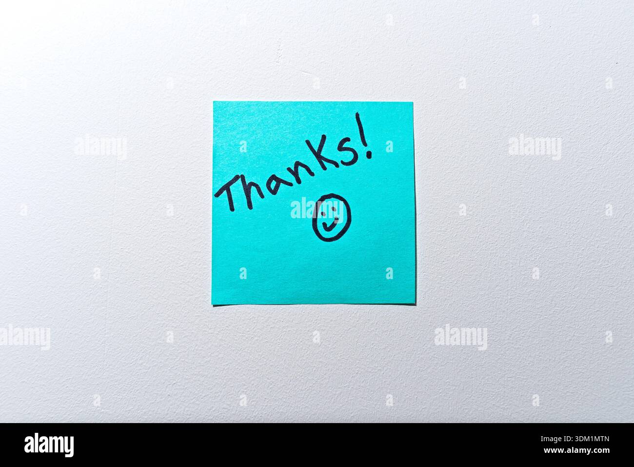 Un simple remerciement manuscrit exprimant sa gratitude est écrit au marqueur noir sur une note collante turquoise vibrante, accompagnée d'un smiley dessiné à la main Banque D'Images