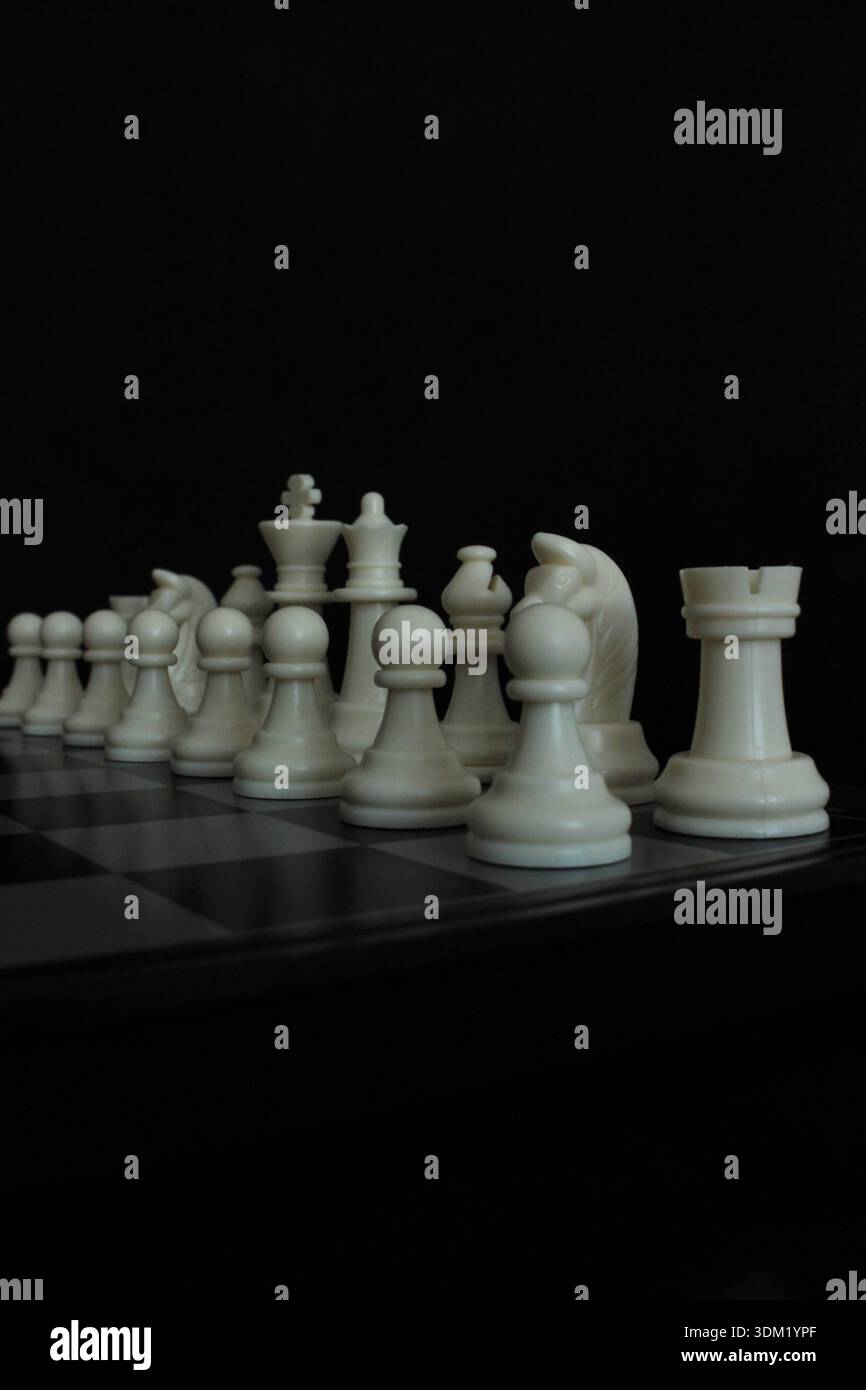 Échiquier sur fond noir avec des pièces d'échecs blanches disposées sur le plateau, symbolisant la stratégie, le leadership et la compétition intellectuelle. Banque D'Images