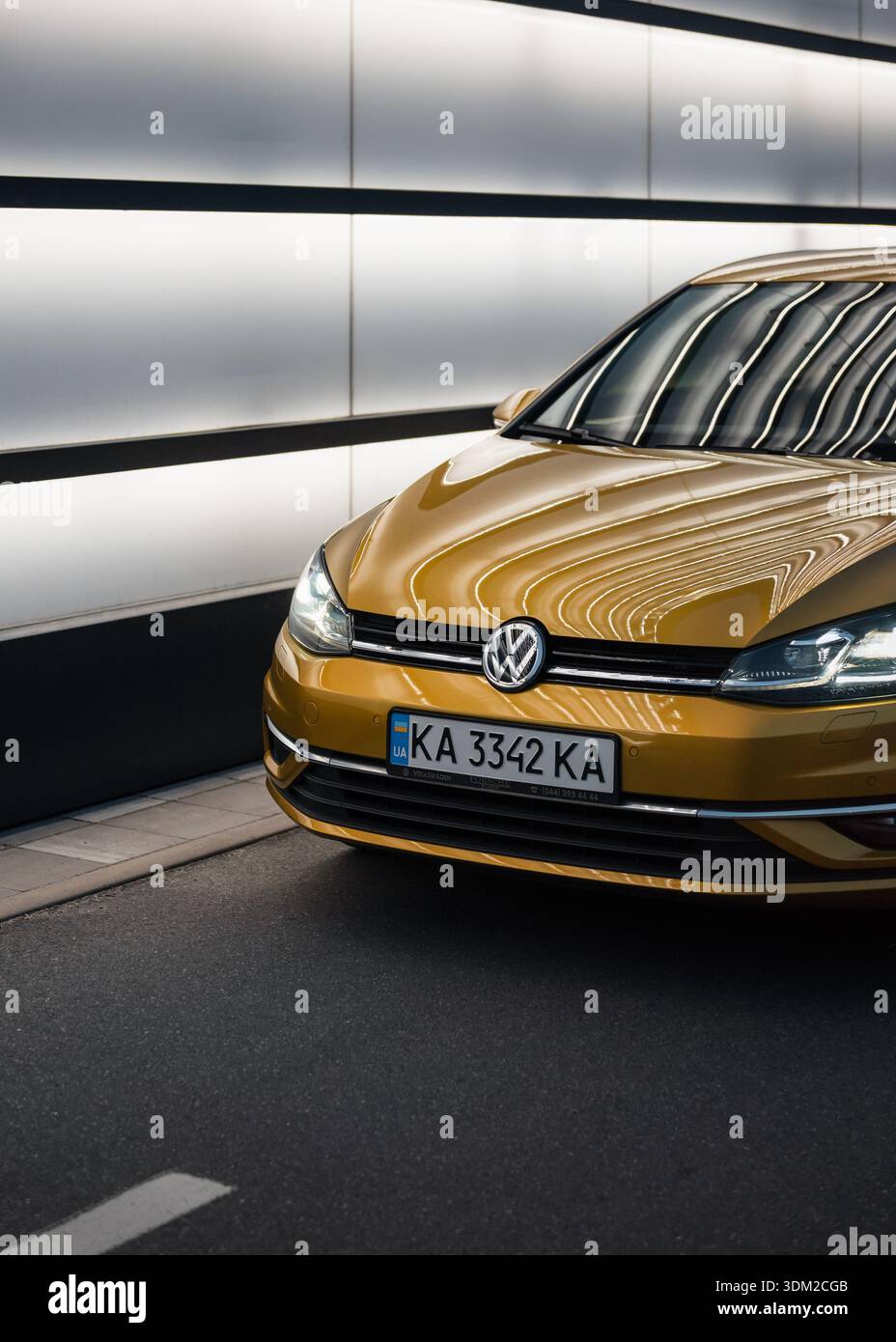 Amber Volkswagen Golf dans une rue avec un mur blanc brillant. Coin avant de la voiture moderne VW hatchback la nuit. Banque D'Images
