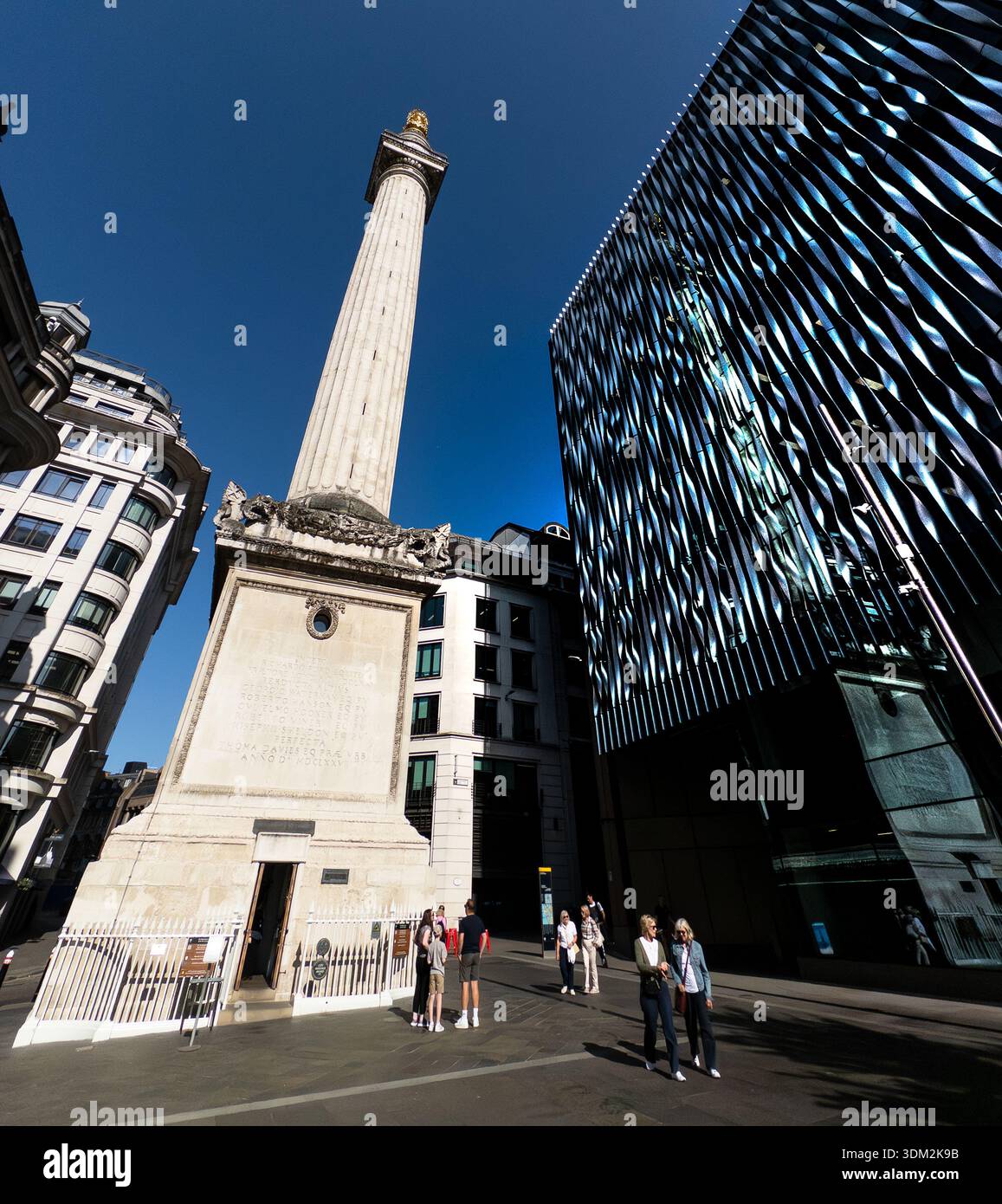 Colonne dorique imposante du Monument au Grand incendie de Londres à côté d'un gratte-ciel moderne en verre ondulé, les touristes se promenant sous un ciel bleu - Image de stock capturée avec un smartphone