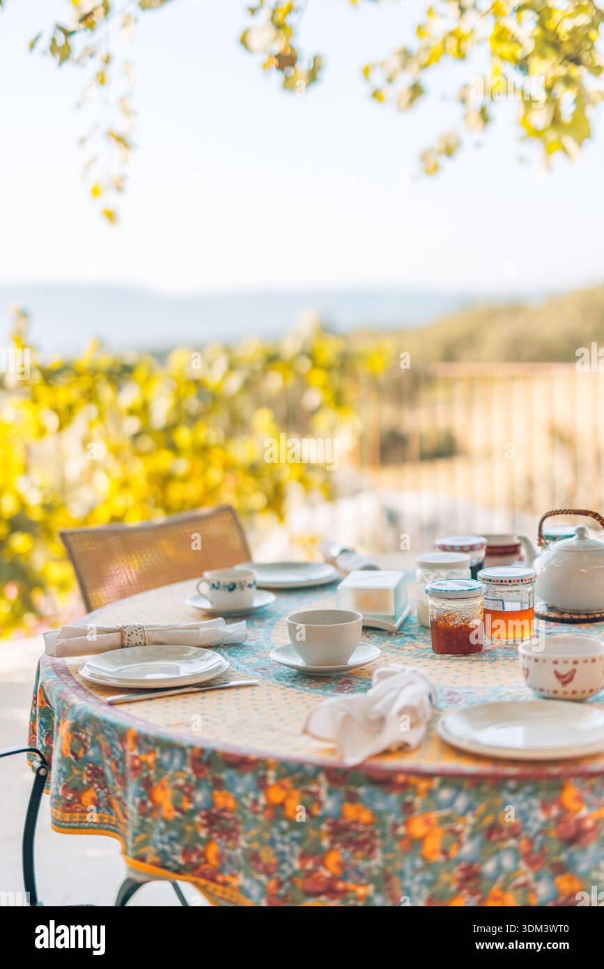 Matin table de petit déjeuner confortable dans la campagne méditerranéenne, ambiance relaxante idyllique, feuillage flou, paysage extérieur paisible Banque D'Images