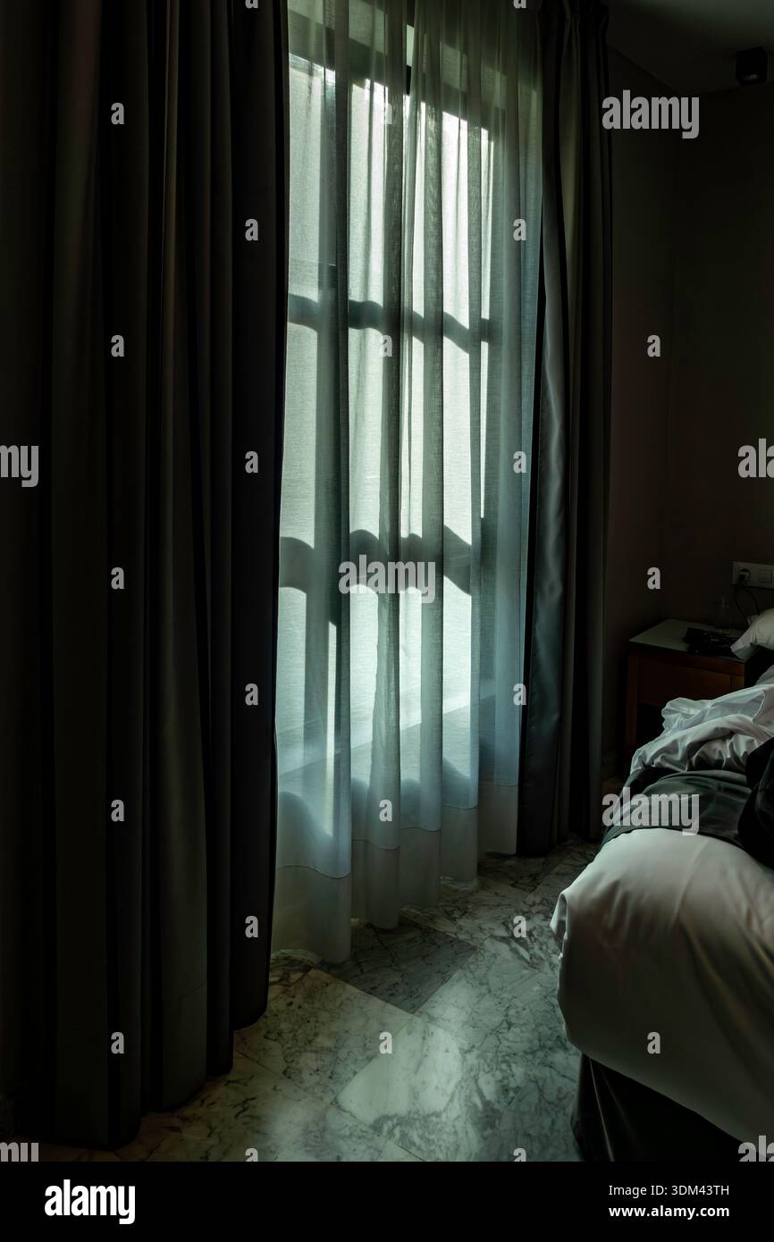 La lumière douce du matin filtre à travers des rideaux blancs et des rideaux sombres dans une chambre d'hôtel, projetant des ombres sur un sol en marbre à Valence, en Espagne. Banque D'Images