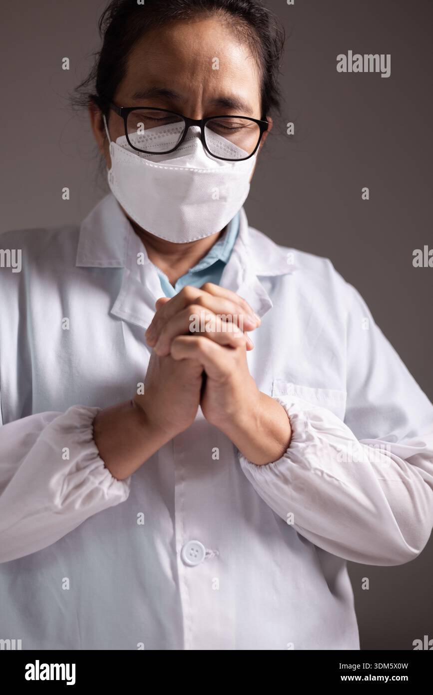 Femme prie avec ses mains serrées, croyant aux soins des médecins et des professionnels de la santé comme elle fait face à la maladie dans un hôpital ou une clinique, confiante Banque D'Images