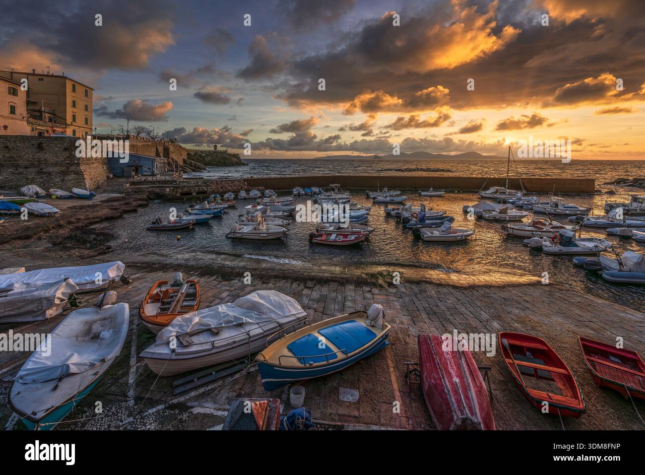 Bateaux de pêche dans le vieux port de Piombino au coucher du soleil. Vue panoramique avec le phare de Piazza Bovio et l'île d'Elbe à l'horizon, Toscane, Italie Banque D'Images