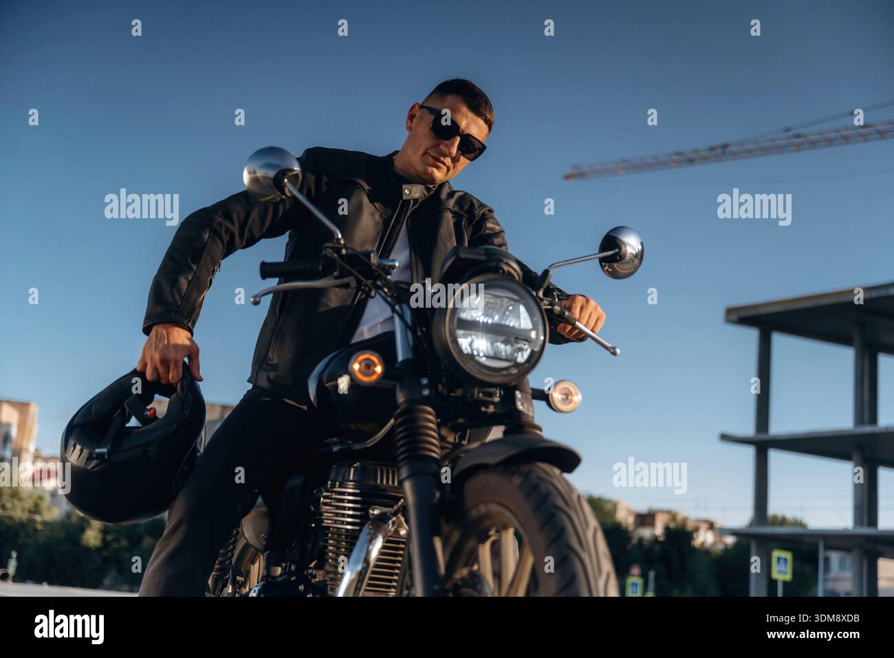 Contre le ciel dégagé, en lunettes de soleil. L'homme est dehors avec sa moto. Banque D'Images