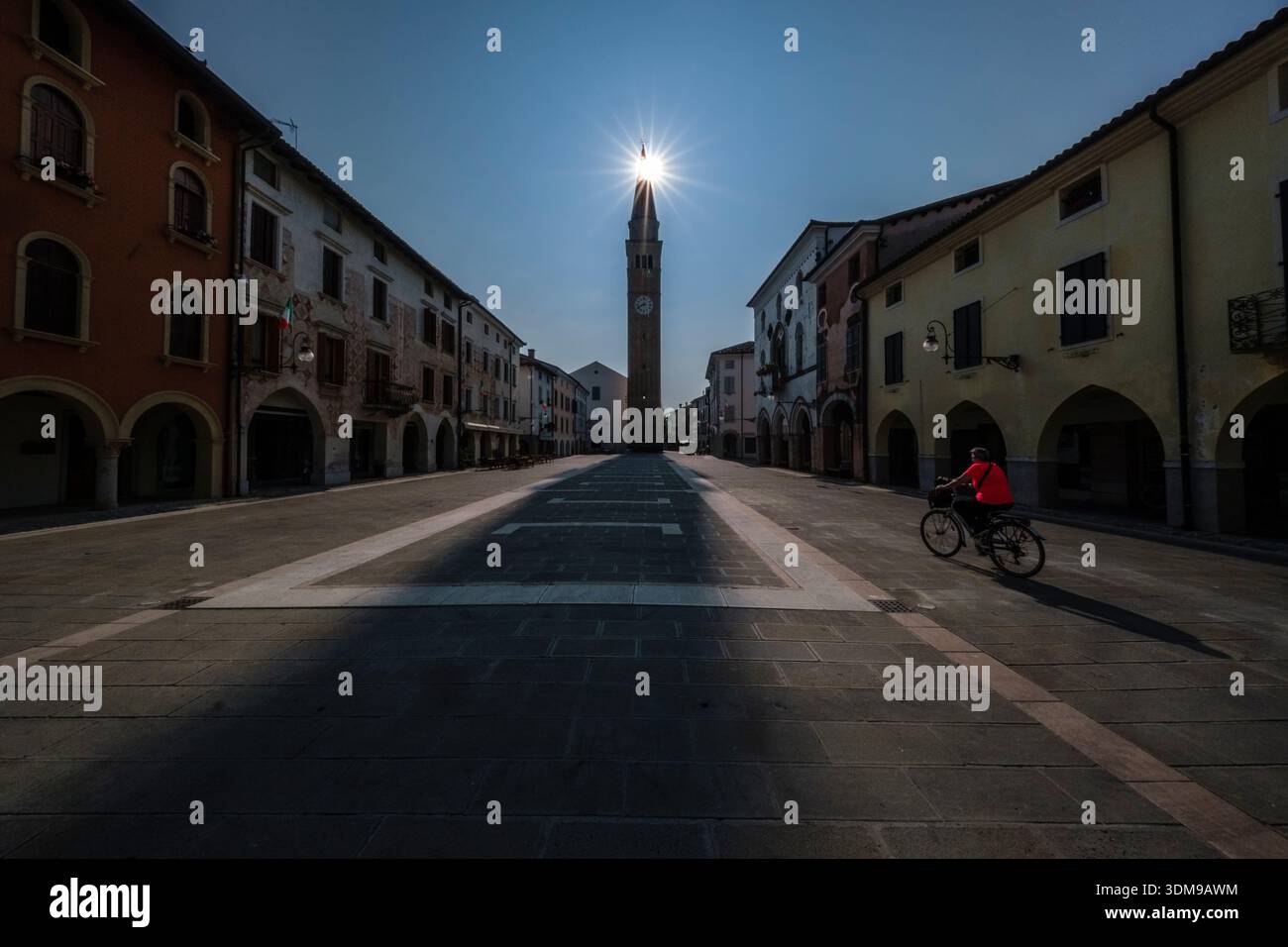Étoile du soleil sur la tour médiévale Torre Raimonda à Piazza del Popolo avec des bâtiments historiques et des fusées éclairantes à San Vito al Tagliamento. Banque D'Images