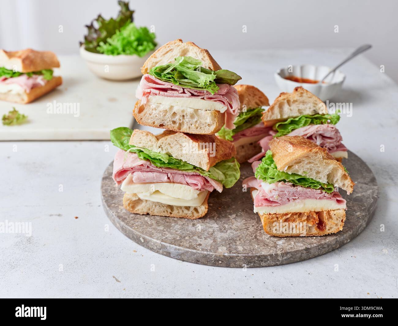 Sandwichs fraîchement préparés empilés sur un plateau en pierre. Les ingrédients comprennent baguette, fromage mozzarella, jambon, laitue et sauce tomate. Banque D'Images