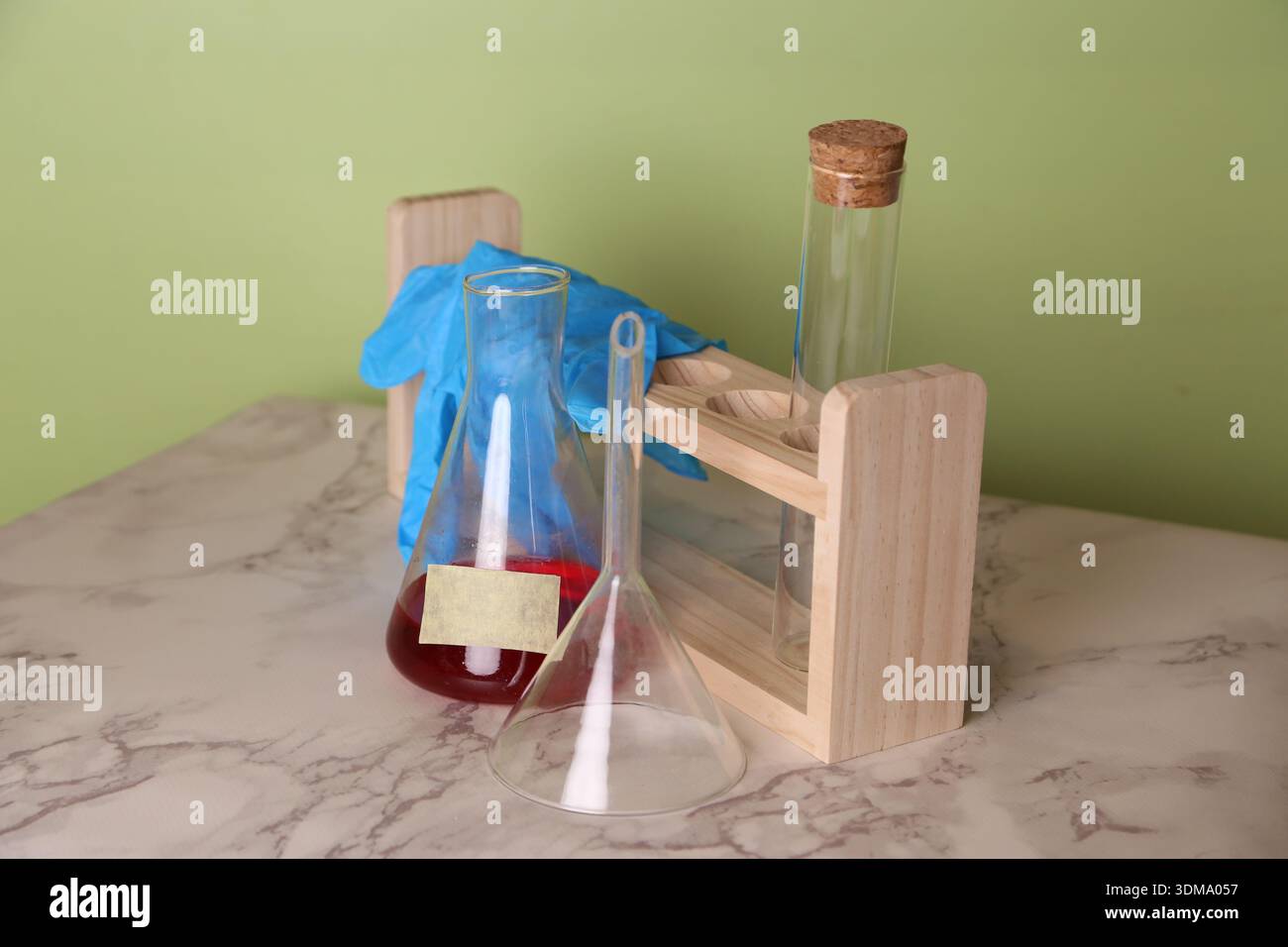 Une variété d'équipements de laboratoire en verre est disposée sur une table en marbre. Il y a deux flacons et un bécher avec du liquide rouge, avec des gants bleus près de b Banque D'Images
