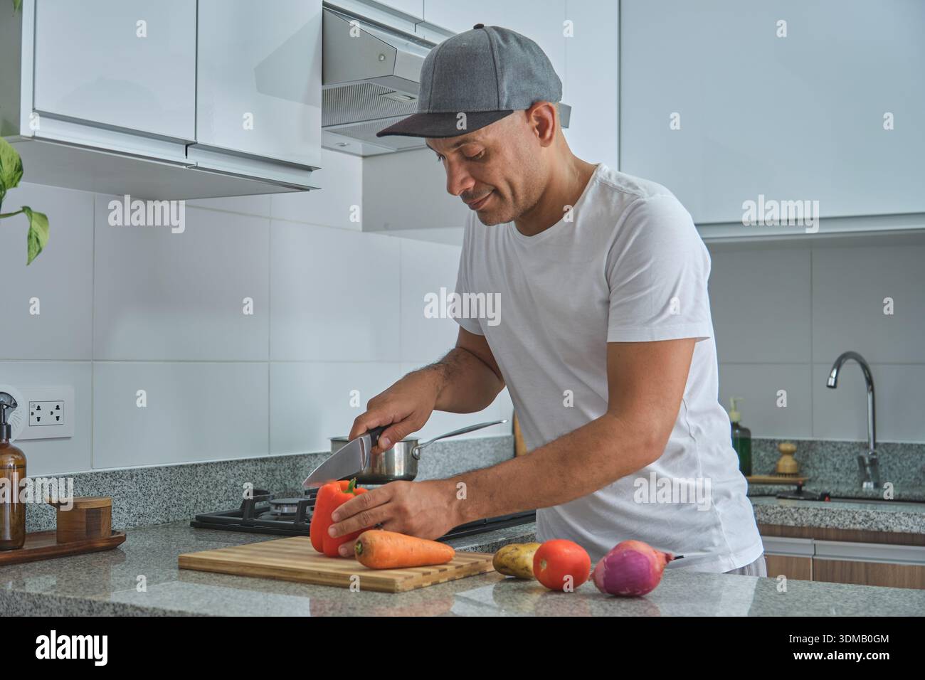 Homme tranchant des légumes sur une planche à découper, préparant un repas sain dans une cuisine moderne Banque D'Images