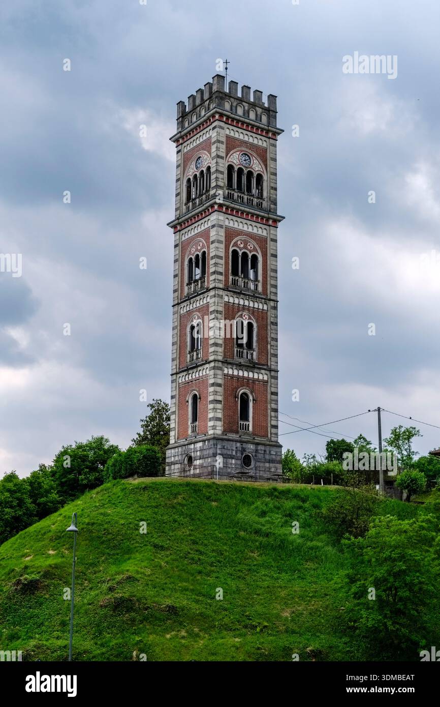 Néo-gothique Torre di Cassacco avec des motifs de briques rouges sur une colline verte sous un ciel nuageux, entourée d'arbres. Banque D'Images