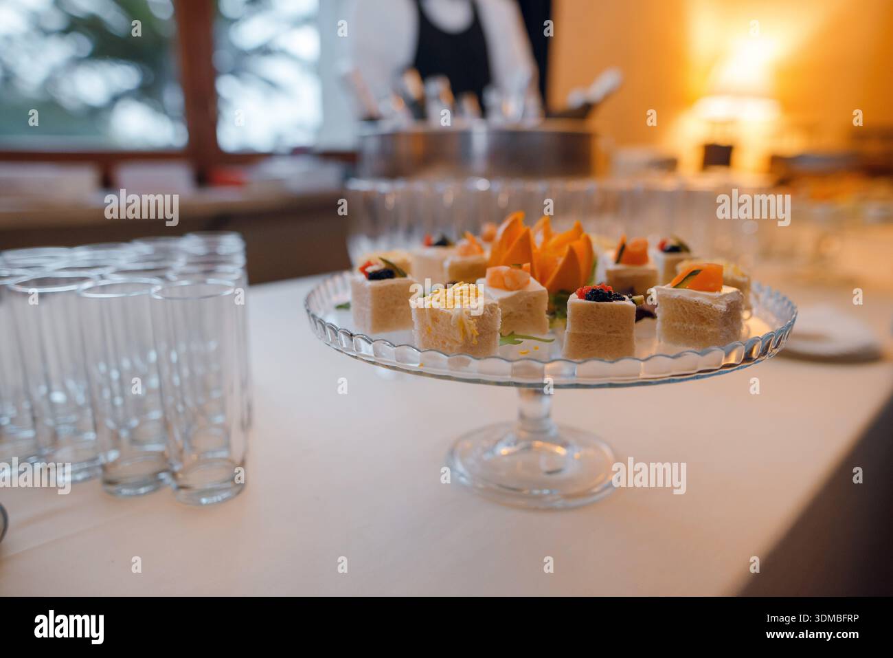 Une sélection de délicats amuse-gueules et canapés sont magnifiquement disposés sur un plateau en verre à plusieurs niveaux, prêt pour les invités lors d'un événement Banque D'Images