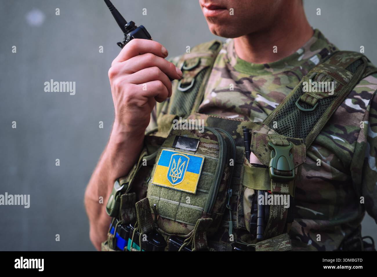 Soldat ukrainien en gilet de camouflage tenant une radio militaire pendant la guerre en Ukraine. Gros plan de l'équipement tactique avec insigne national, symbolisant Banque D'Images