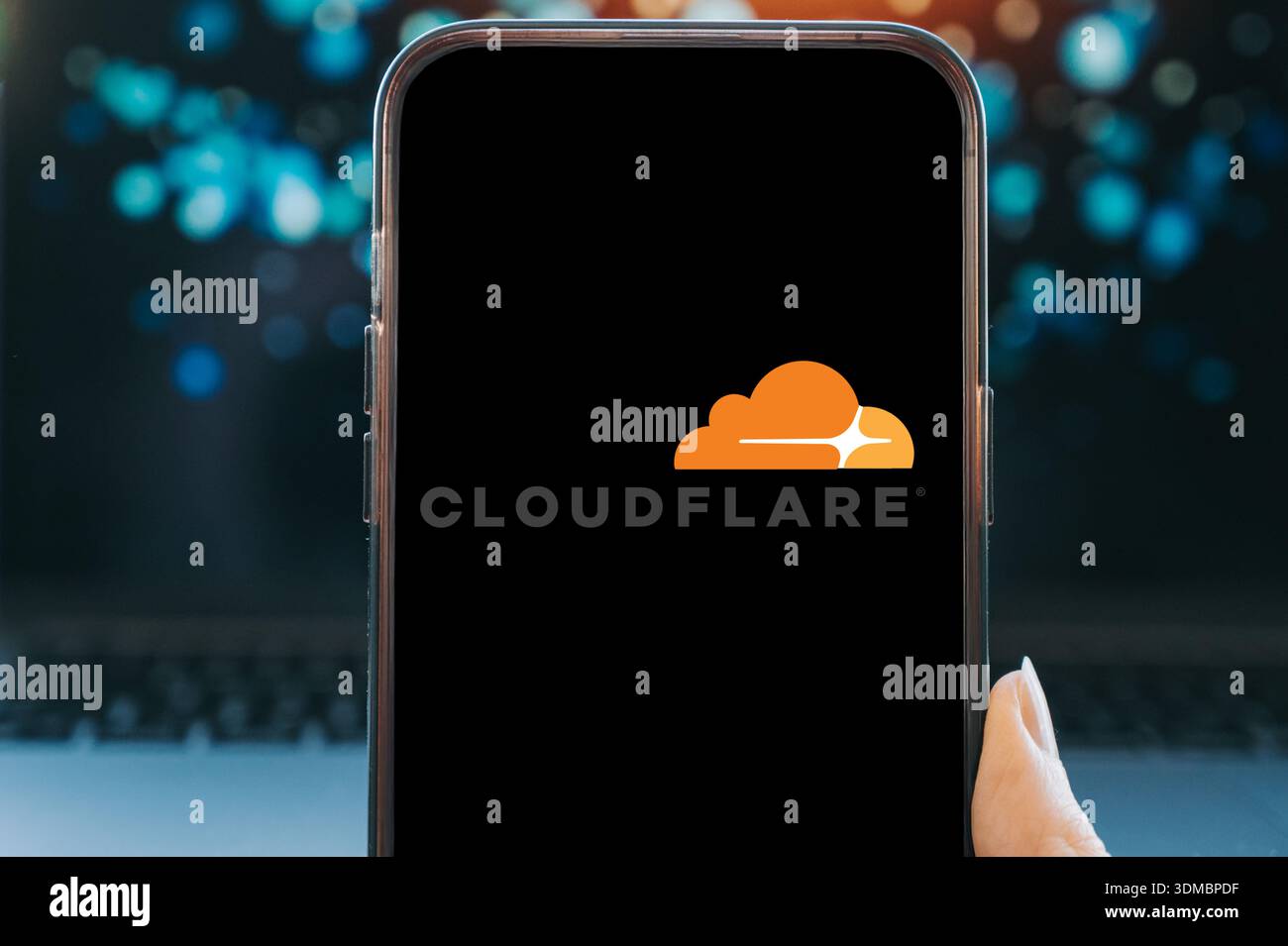Smartphone affichant le logo Cloudflare sur un écran noir, tenu en main sur un fond technologique flou. Image conceptuelle représentant Cloud co Banque D'Images