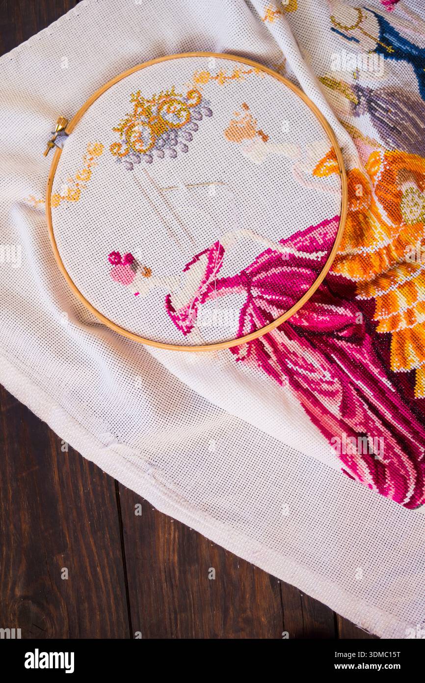 Broderie artisanale avec fil coloré sur tissu. Ciseaux, aiguille et un coussin d'épingle sont placés à proximité, mettant l'accent sur l'artisanat et le processus de travail à l'aiguille Banque D'Images