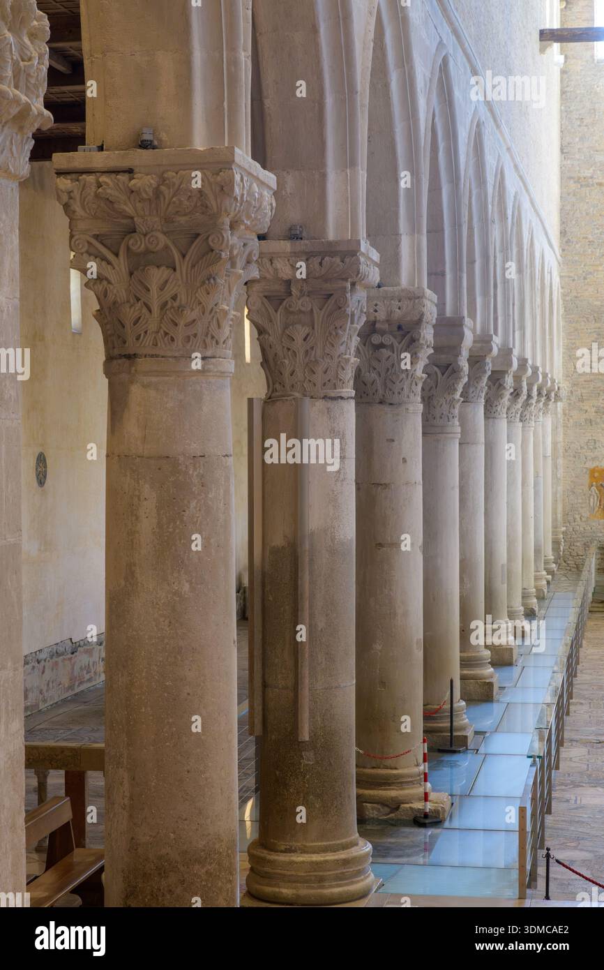 Intérieur de la Basilique d'Aquilée (Basilica di Aquileia), Italie. Rangée de colonnes de pierre avec des chapiteaux et passerelle en verre au-dessus de mosaïques anciennes. Banque D'Images